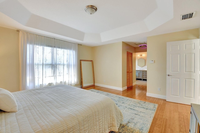 bedroom with a raised ceiling, light wood-type flooring, and ensuite bathroom