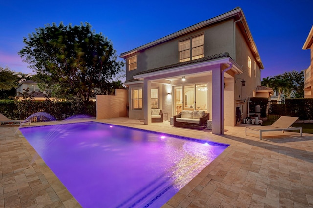 pool at dusk featuring pool water feature, a patio, ceiling fan, and an outdoor hangout area