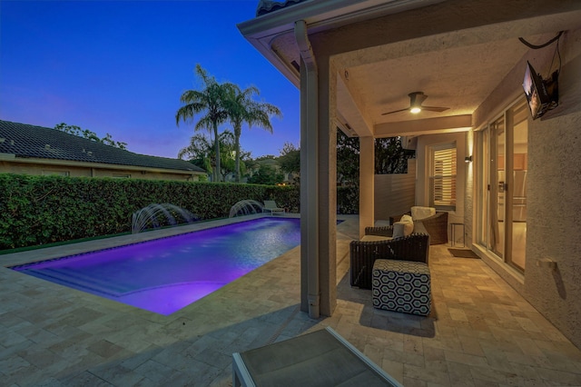 pool at dusk featuring pool water feature, ceiling fan, and a patio area