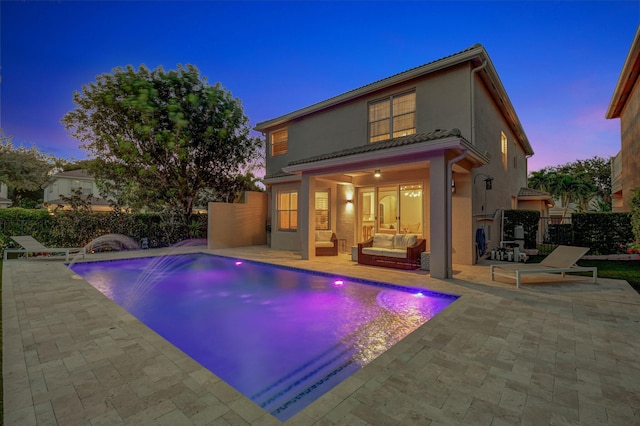 pool at dusk with a patio, outdoor lounge area, and pool water feature