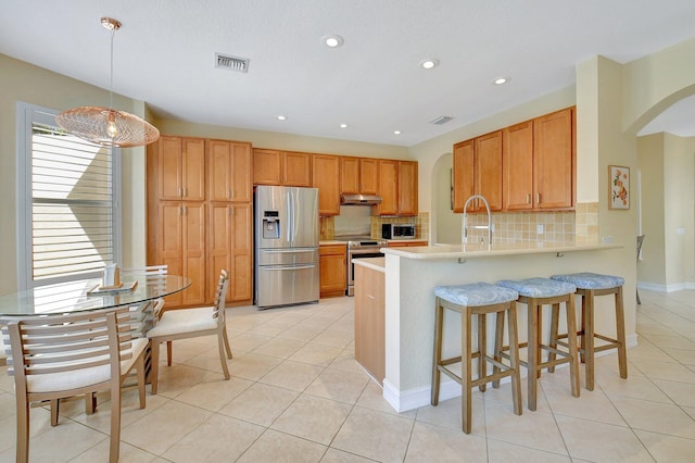 kitchen featuring hanging light fixtures, kitchen peninsula, tasteful backsplash, stainless steel appliances, and a breakfast bar