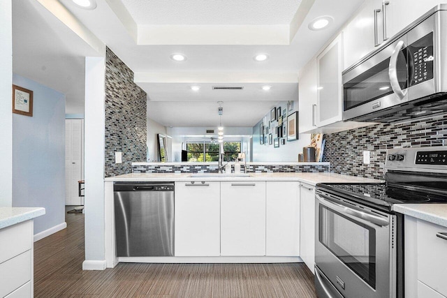 kitchen featuring backsplash, kitchen peninsula, white cabinetry, and stainless steel appliances