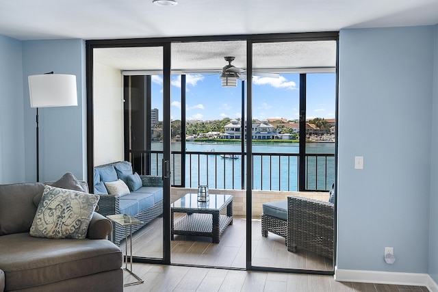 living room featuring hardwood / wood-style floors, a water view, ceiling fan, and expansive windows