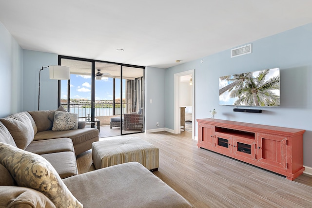 living room with floor to ceiling windows, light wood finished floors, visible vents, a ceiling fan, and baseboards