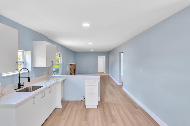 kitchen featuring kitchen peninsula, white cabinetry, sink, and light hardwood / wood-style flooring