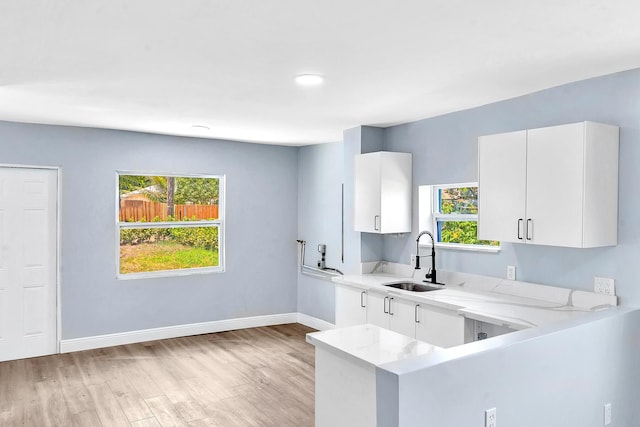 kitchen with kitchen peninsula, light stone counters, sink, and white cabinets