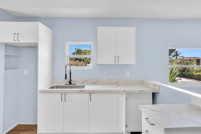 kitchen with hardwood / wood-style floors, light stone counters, white cabinetry, and sink