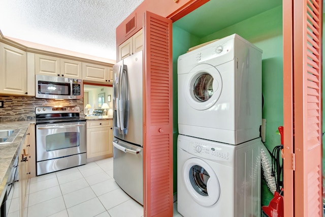 washroom with a textured ceiling, light tile patterned floors, and stacked washer and clothes dryer