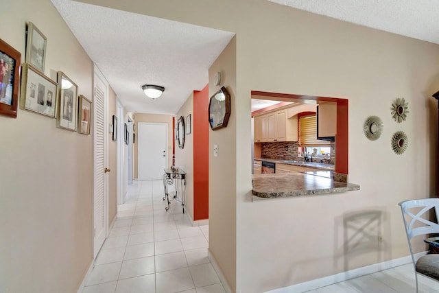 hall with a textured ceiling, light tile patterned floors, and sink