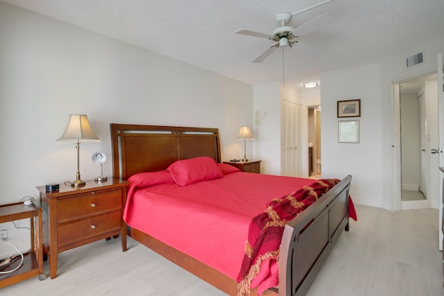 bedroom with ceiling fan, a textured ceiling, light hardwood / wood-style flooring, and a closet