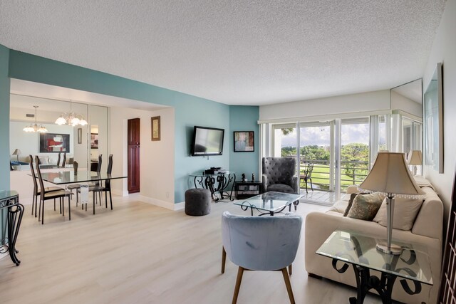 living area with light wood-style floors, a textured ceiling, baseboards, and a notable chandelier