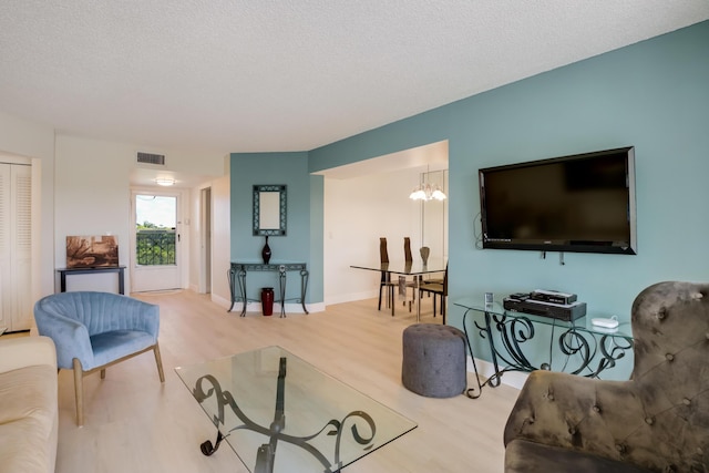 living area with a textured ceiling, visible vents, baseboards, an inviting chandelier, and wood finished floors