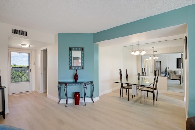 dining space featuring light wood-type flooring, visible vents, a textured ceiling, and a notable chandelier