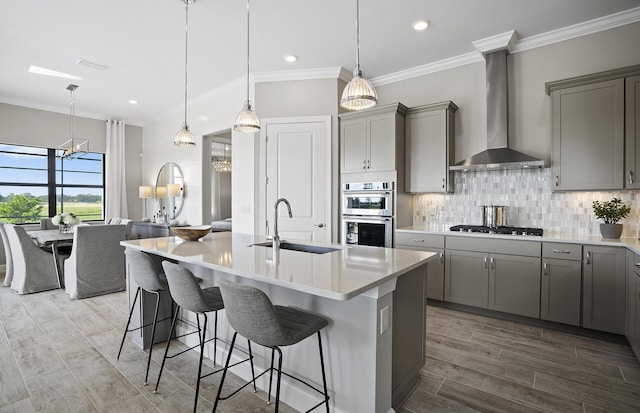 kitchen with wall chimney exhaust hood, sink, a breakfast bar area, double oven, and a kitchen island with sink