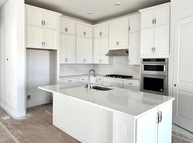 kitchen with wall chimney exhaust hood, sink, decorative light fixtures, gray cabinets, and an island with sink