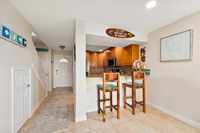 kitchen with light tile patterned flooring, kitchen peninsula, a kitchen breakfast bar, backsplash, and appliances with stainless steel finishes