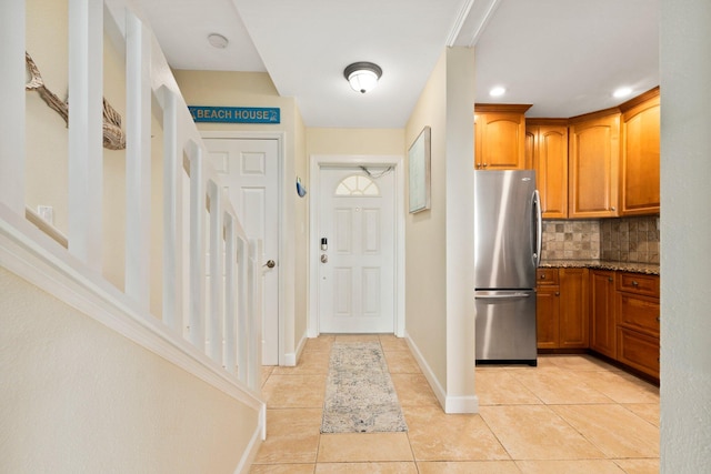 kitchen with decorative backsplash, light tile patterned floors, stone counters, and stainless steel refrigerator