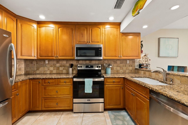 kitchen with appliances with stainless steel finishes, light tile patterned flooring, light stone counters, tasteful backsplash, and sink