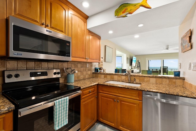 kitchen featuring light stone counters, tasteful backsplash, stainless steel appliances, ceiling fan, and sink