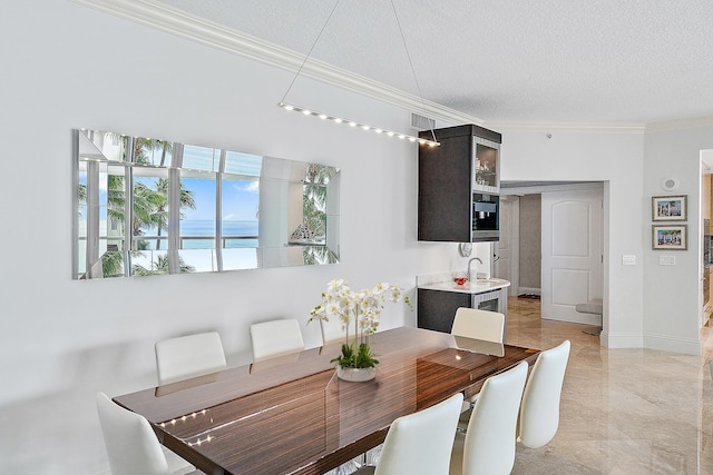 dining space with sink, a water view, ornamental molding, and a textured ceiling