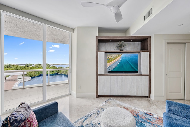 living room with ceiling fan, a water view, and a wealth of natural light