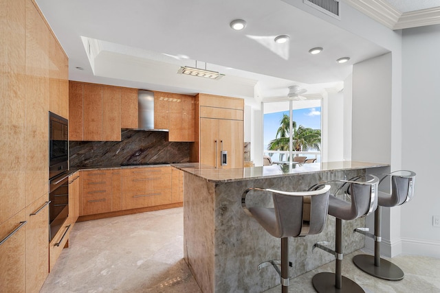 kitchen featuring dark stone counters, wall chimney exhaust hood, a breakfast bar, crown molding, and built in appliances