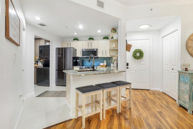 kitchen featuring light wood-type flooring, white cabinetry, kitchen peninsula, appliances with stainless steel finishes, and light stone countertops