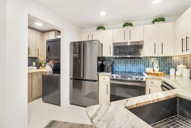 kitchen featuring appliances with stainless steel finishes, stacked washer and clothes dryer, backsplash, and light tile patterned floors