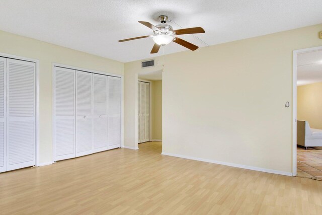 unfurnished bedroom with ceiling fan, multiple closets, a textured ceiling, and light wood-type flooring