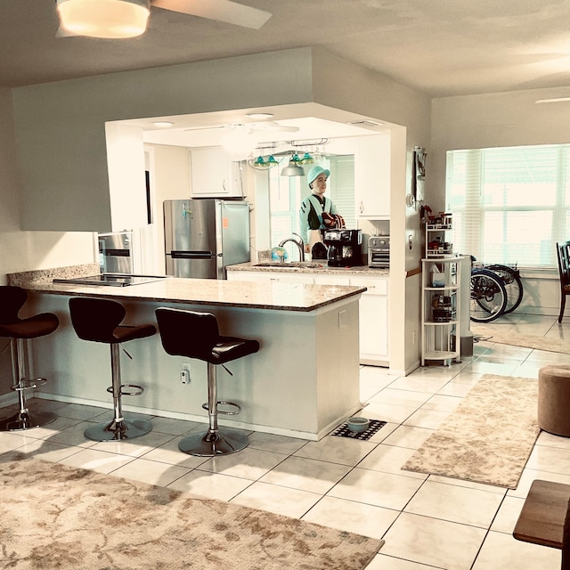 kitchen featuring light tile patterned flooring, stainless steel fridge, a breakfast bar, kitchen peninsula, and white cabinetry