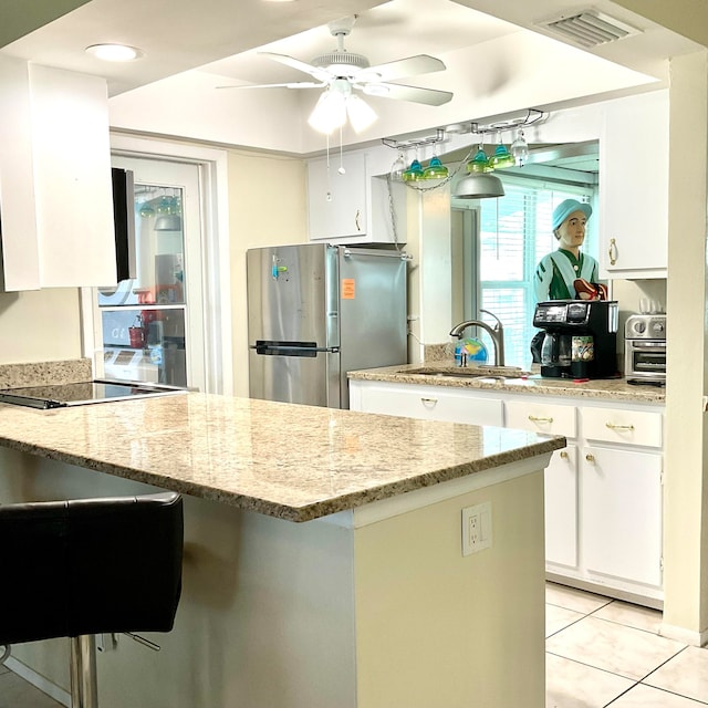 kitchen featuring light stone counters, stainless steel refrigerator, sink, and white cabinetry