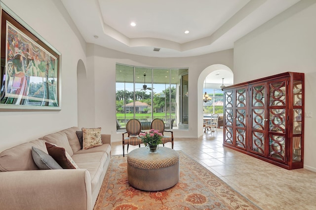 tiled living room featuring a tray ceiling and a notable chandelier