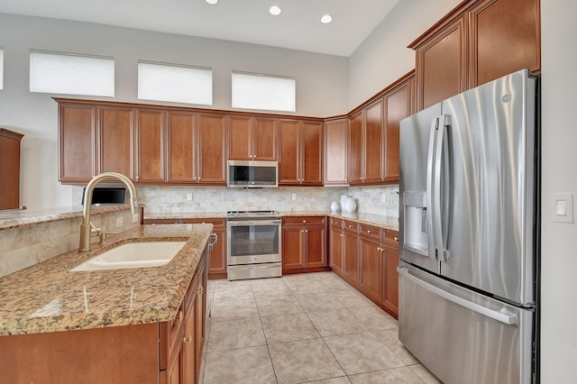 9772 Via Grandezza W, Wellington, FL 33411 - kitchen with a sink, tasteful backsplash, light stone counters, brown cabinetry, and appliances with stainless steel finishes