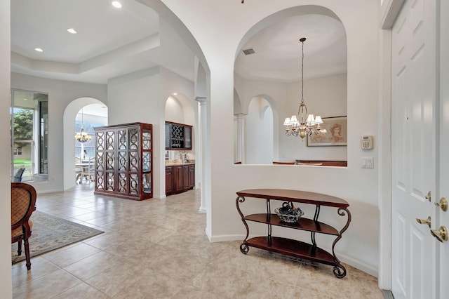 corridor featuring a tray ceiling, light tile patterned floors, and a notable chandelier