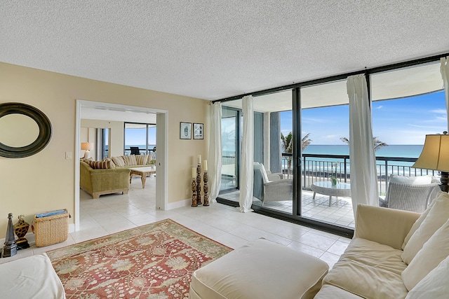 tiled living room featuring a textured ceiling, a water view, and a wall of windows