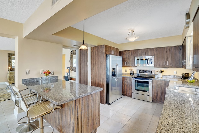 kitchen featuring pendant lighting, stone counters, sink, a textured ceiling, and appliances with stainless steel finishes