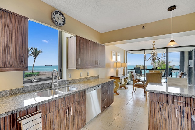 kitchen featuring light stone counters, stainless steel dishwasher, sink, pendant lighting, and a water view