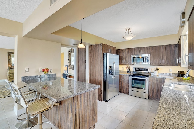 kitchen with stone countertops, sink, hanging light fixtures, stainless steel appliances, and a kitchen bar