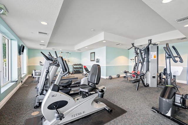 workout area featuring a tray ceiling and a textured ceiling