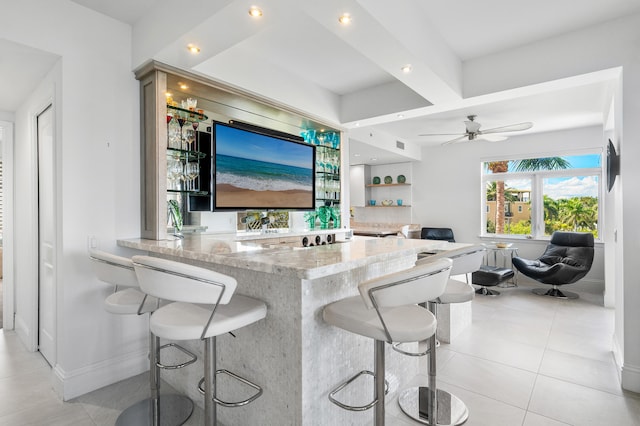 kitchen with a breakfast bar, light stone counters, kitchen peninsula, light tile patterned floors, and ceiling fan