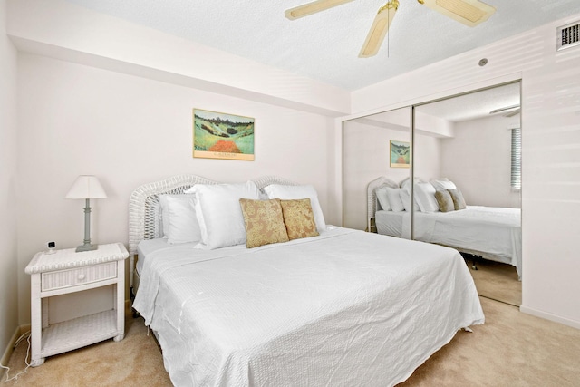 bedroom with light colored carpet, a textured ceiling, ceiling fan, and a closet