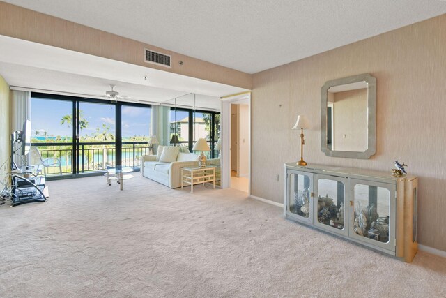 living room featuring light colored carpet, floor to ceiling windows, ceiling fan, and a water view