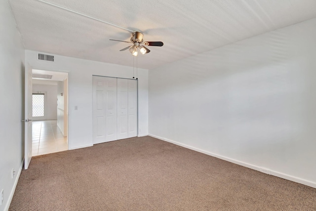 unfurnished bedroom featuring carpet flooring, a textured ceiling, a closet, and ceiling fan