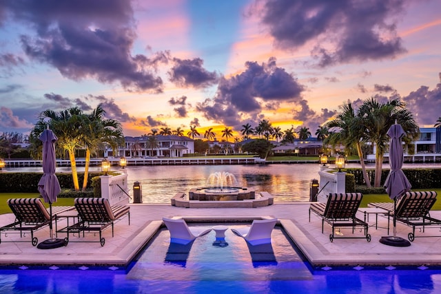 pool at dusk featuring a water view, a patio area, and an outdoor fire pit