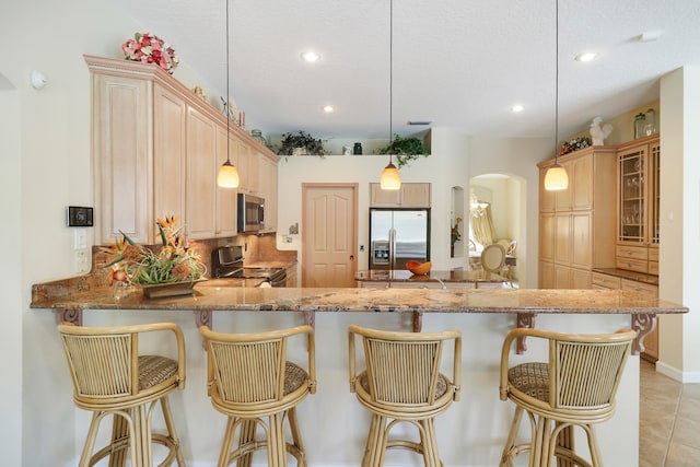 kitchen featuring tasteful backsplash, kitchen peninsula, hanging light fixtures, stainless steel appliances, and light brown cabinets