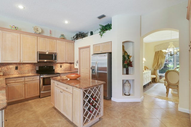kitchen featuring a chandelier, light stone counters, a center island, light tile patterned flooring, and appliances with stainless steel finishes