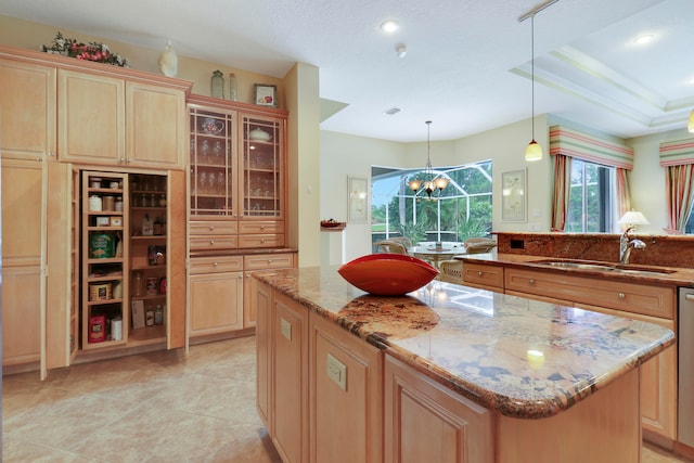 kitchen featuring pendant lighting, sink, a center island, a notable chandelier, and light stone countertops