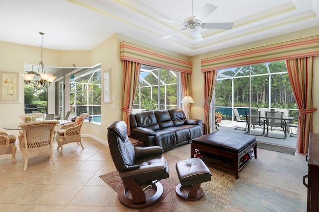 living room featuring ceiling fan with notable chandelier, crown molding, light tile patterned floors, and a tray ceiling