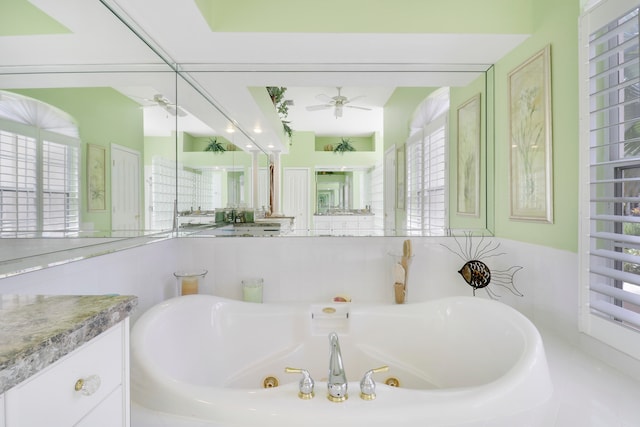 bathroom featuring vanity, ceiling fan, tiled bath, and a healthy amount of sunlight