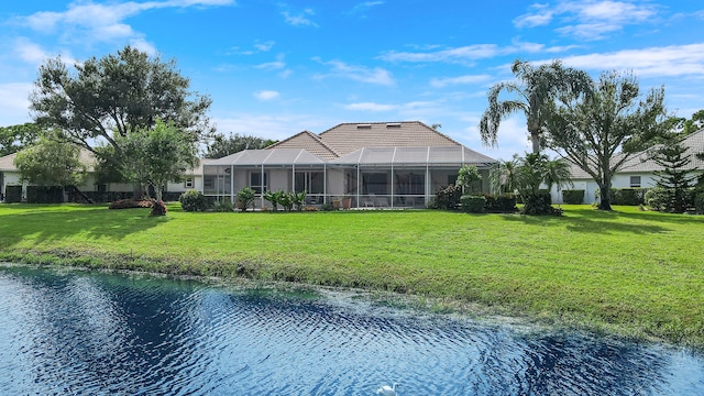 rear view of house featuring glass enclosure, a water view, and a lawn
